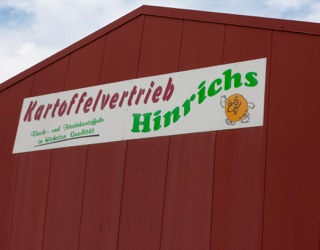 Rotes Gebäude mit einem Firmenschild, auf dem "Kartoffelvertrieb Hinrichs" steht.