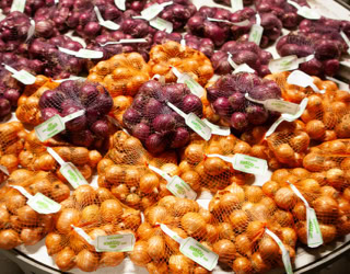 Verschiedene Bündel von Zwiebeln in Netzen, lila und braun, auf einem Tisch ausgestellt.